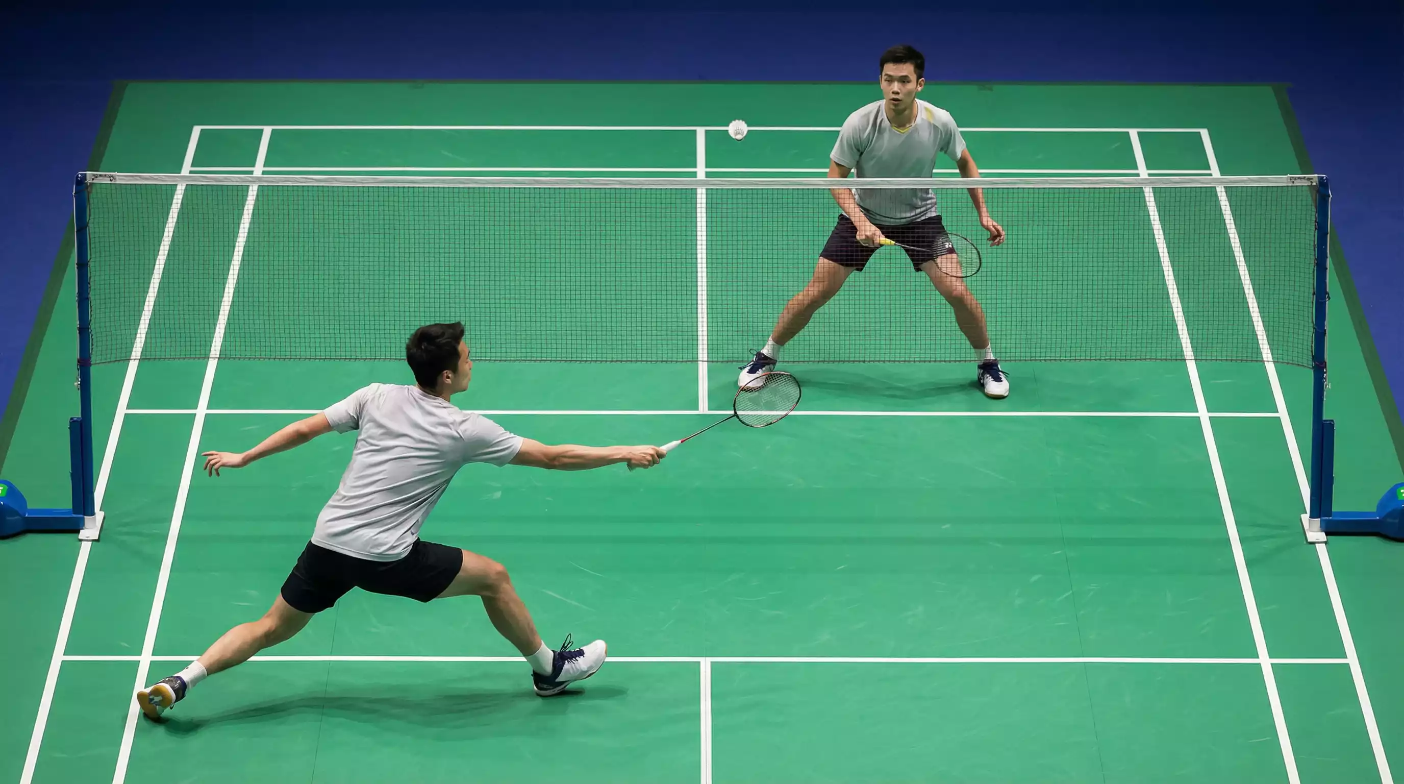 Badminton-Spieler während eines intensiven Ballwechsels in einer Sporthalle